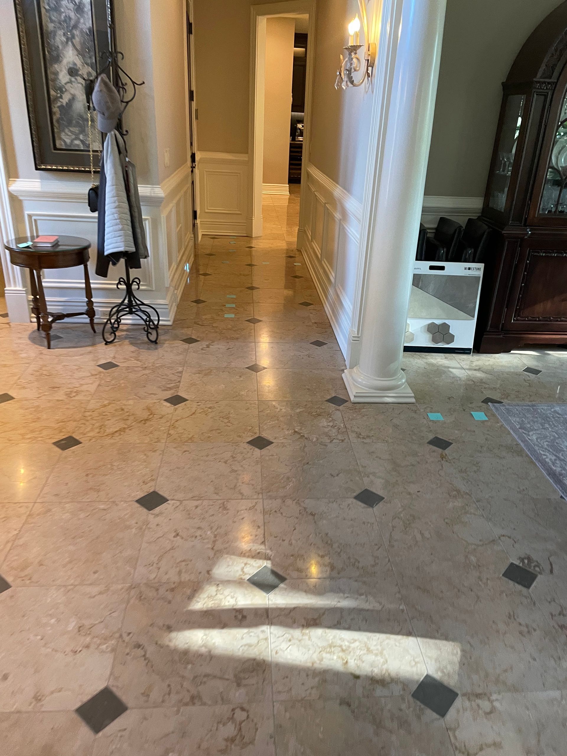 Hallway with marble tile floor, sunlight patches, framed art, and a small table by the wall.