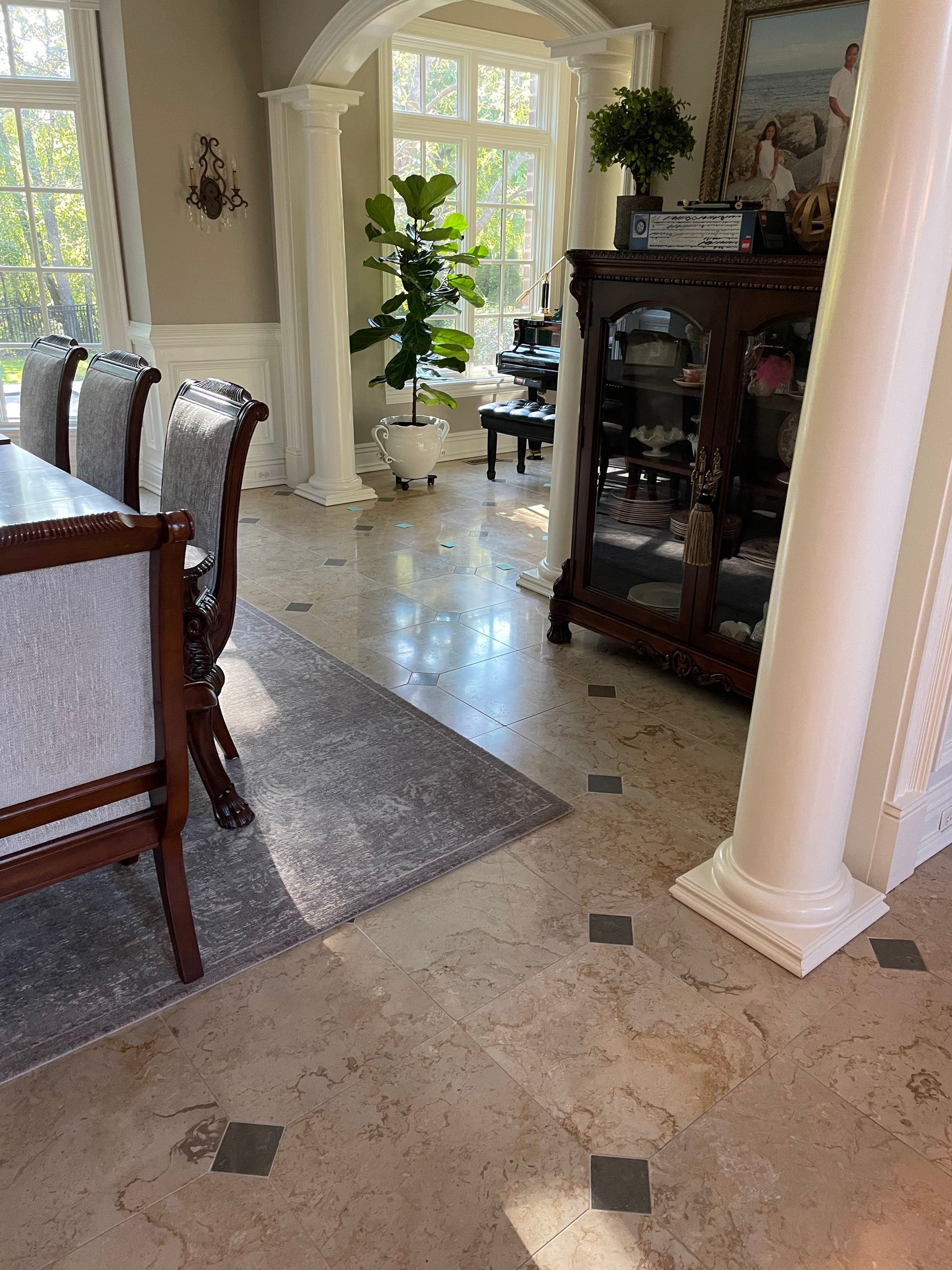 Bright dining room with tiled floor, white columns, wooden chairs, and a glass display cabinet.