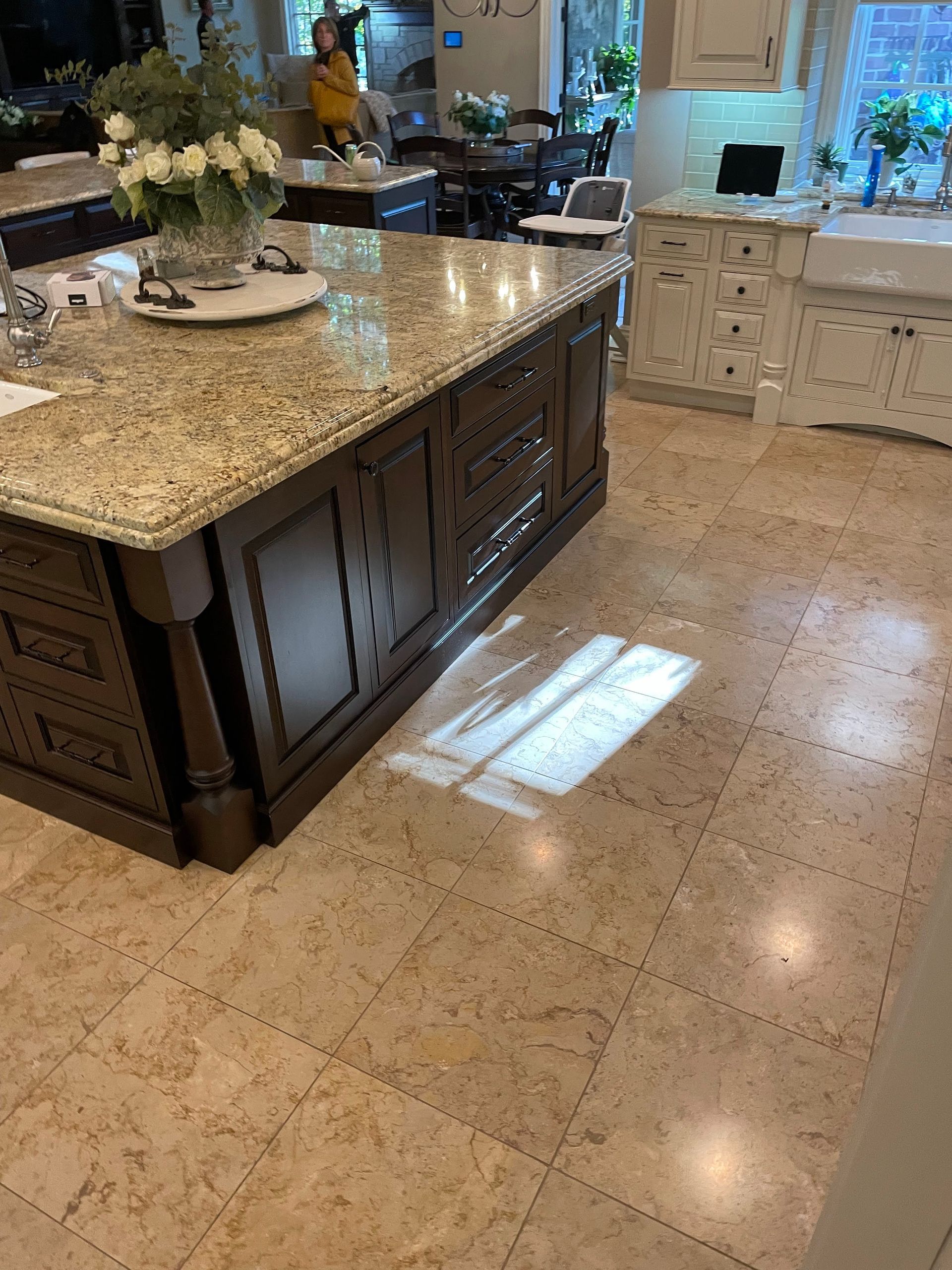 Modern kitchen with large granite island, dark wood cabinets, and sunlit tile floor