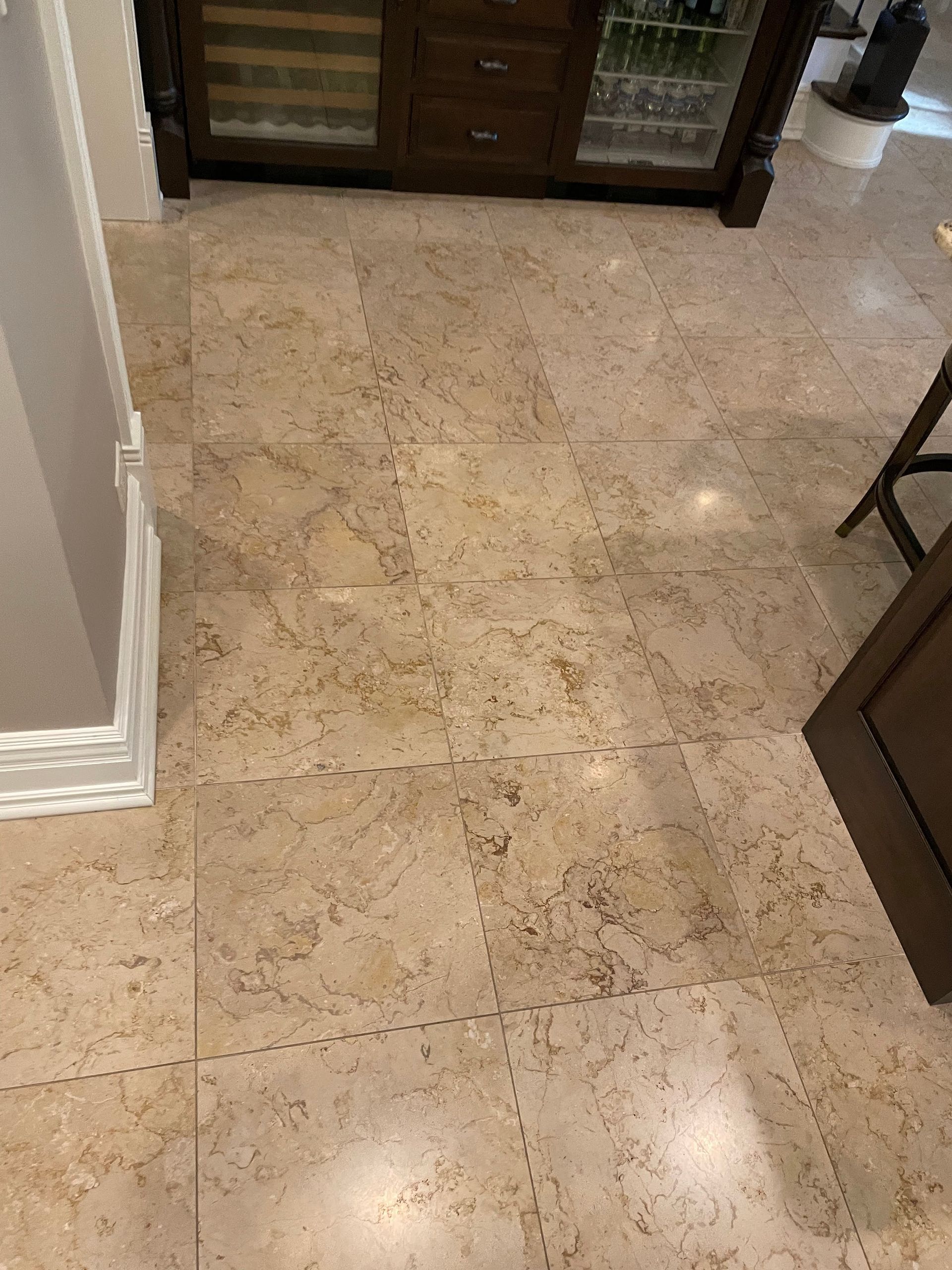 Polished beige tile floor in a hallway near a doorway and furniture.