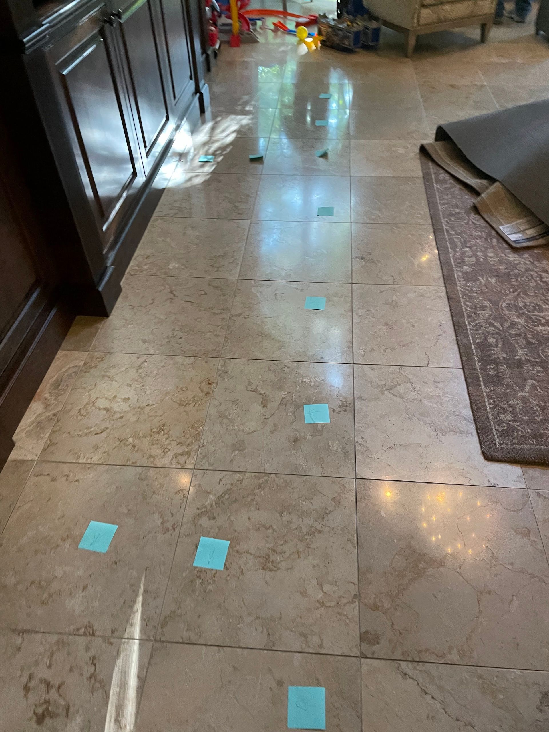 Indoor hallway with polished marble floor marked by blue tape squares, near a rug and doorway.