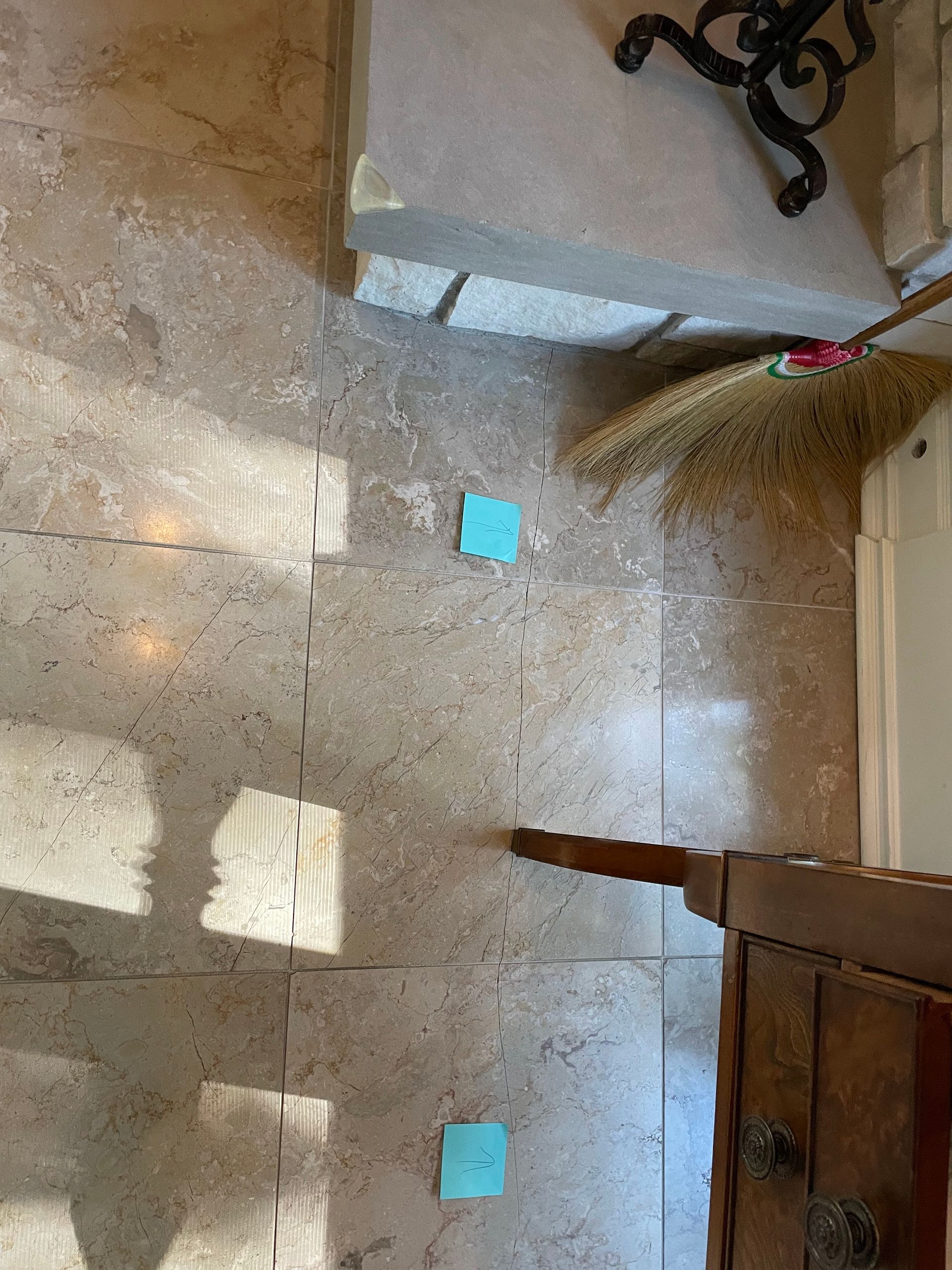 Top-down view of a tiled floor with sunlight patches and two small blue sticky notes near furniture.