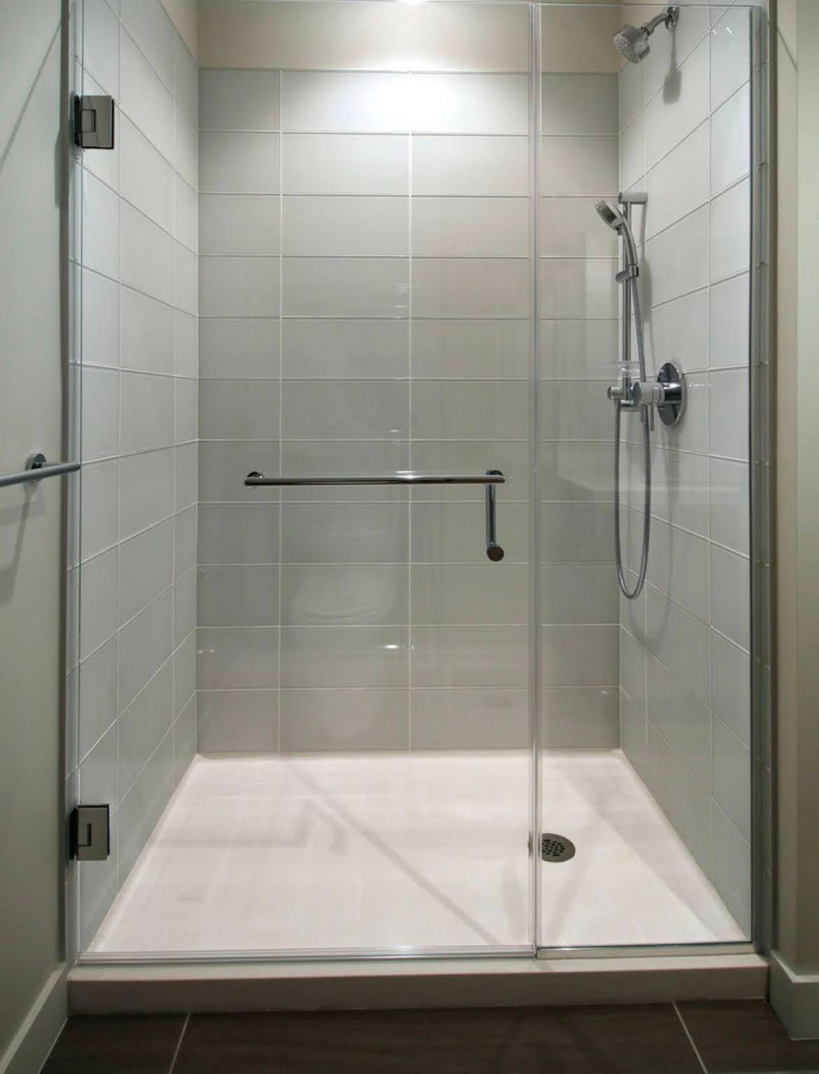 Empty modern glass shower stall with white tiled walls and a grab bar