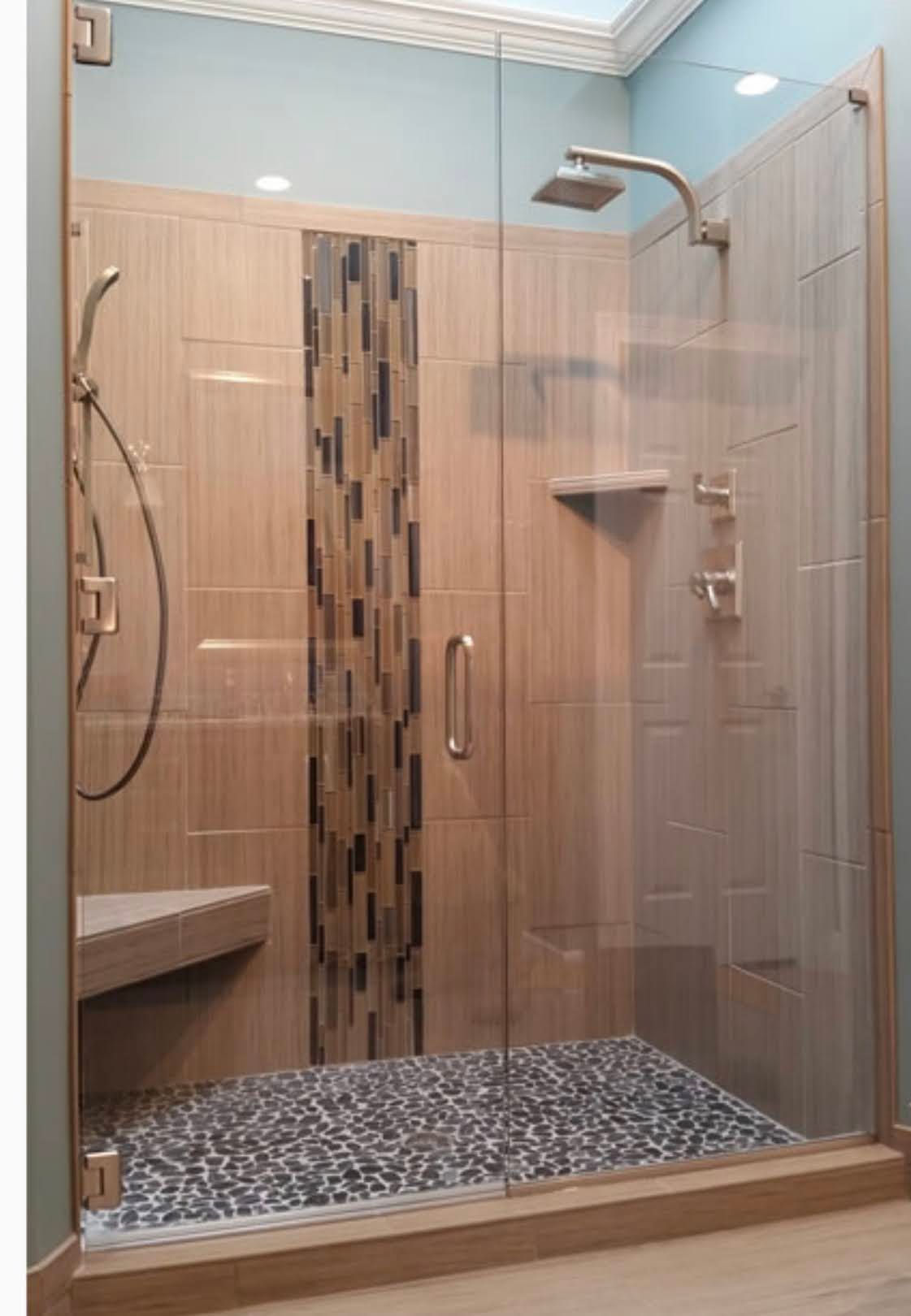 Walk-in shower with clear glass enclosure, mosaic tile floor, and wood panel accent wall