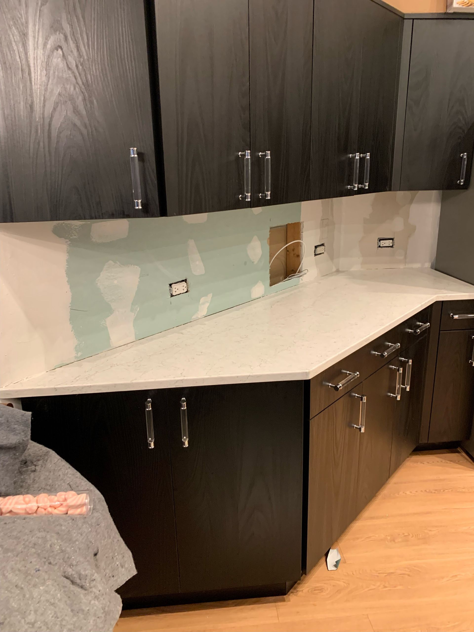 Kitchen with dark cabinets, light countertop, and peeling paint on the mint-green backsplash area.