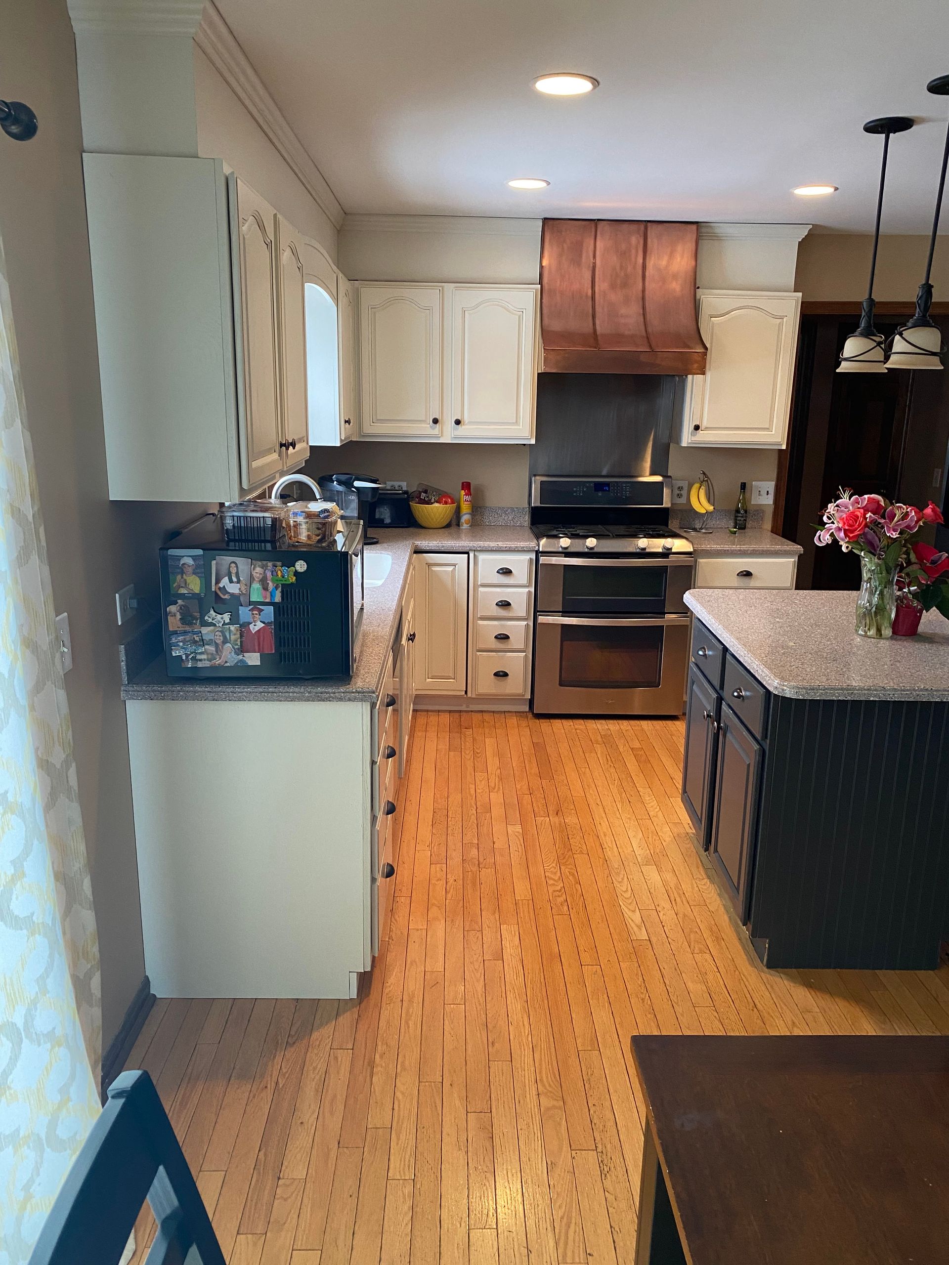 Bright kitchen with white cabinets, wood floor, black appliances, and a granite island viewed from the entryway