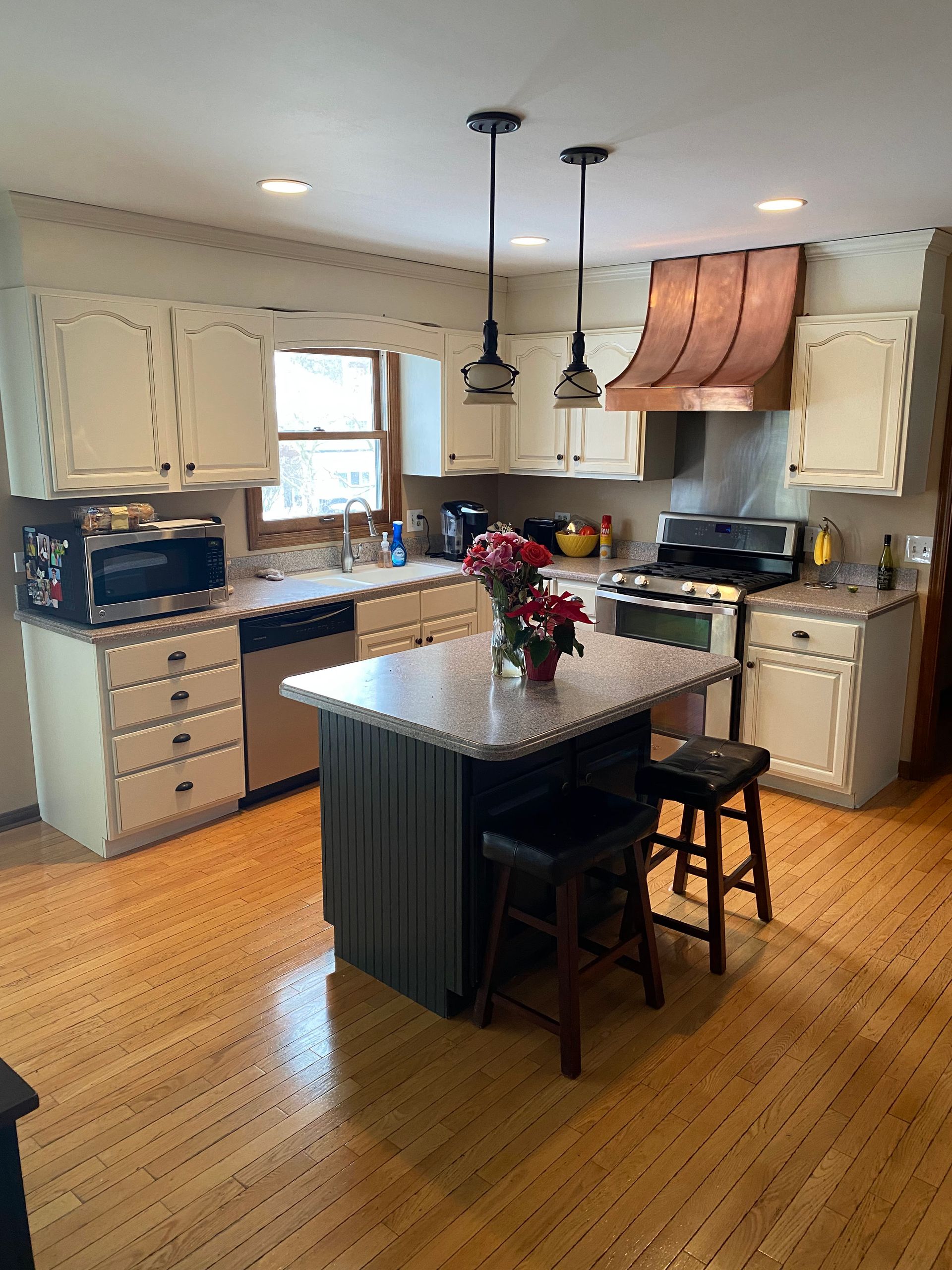 Bright kitchen with central island, wood floors, cream cabinets, and copper range hood.