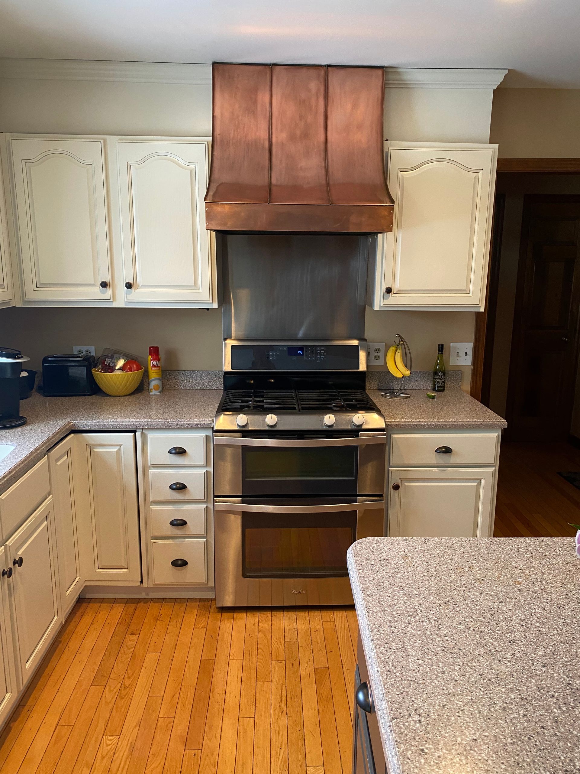 Kitchen with stainless steel stove and copper hood, white cabinets, granite counters, and hardwood floor.