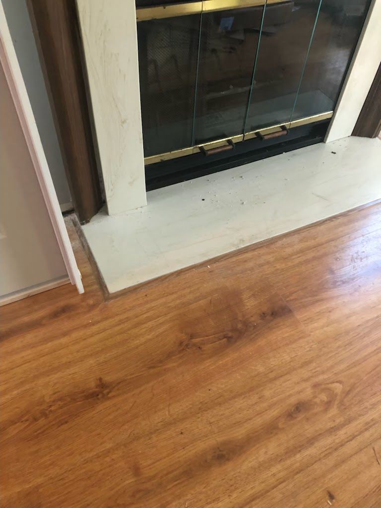 Wooden floor meeting a white fireplace hearth with a dark glass fireplace insert.