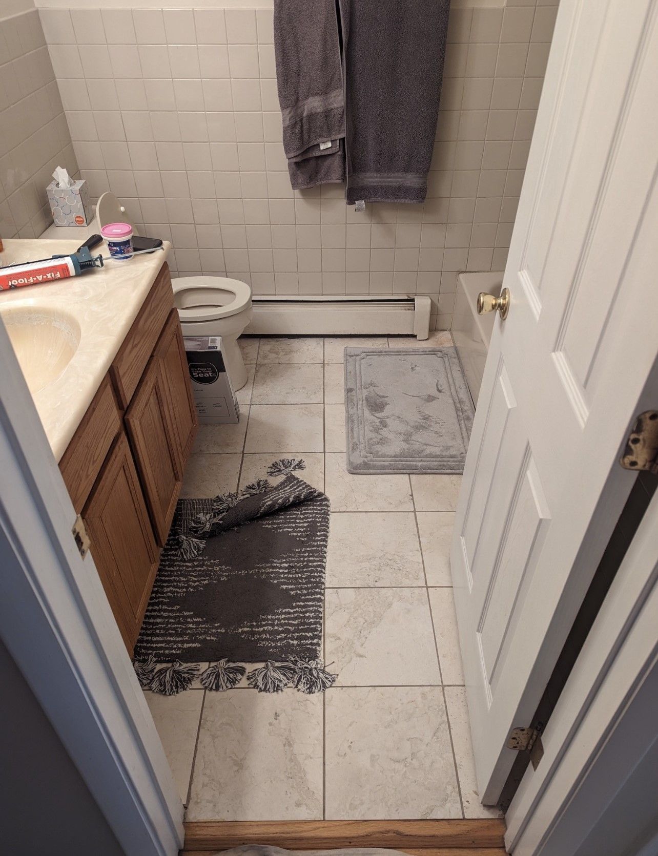 Small bathroom with a sink, toilet, shower curtain, and wet towel on a tiled floor.