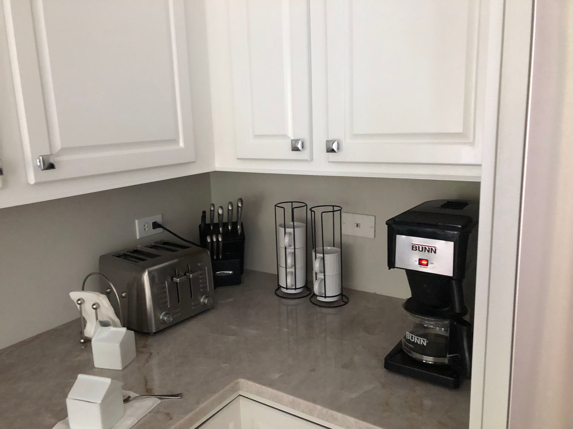Kitchen counter with coffee maker, toaster, knife block, paper towel holder, and spray bottle under white cabinets