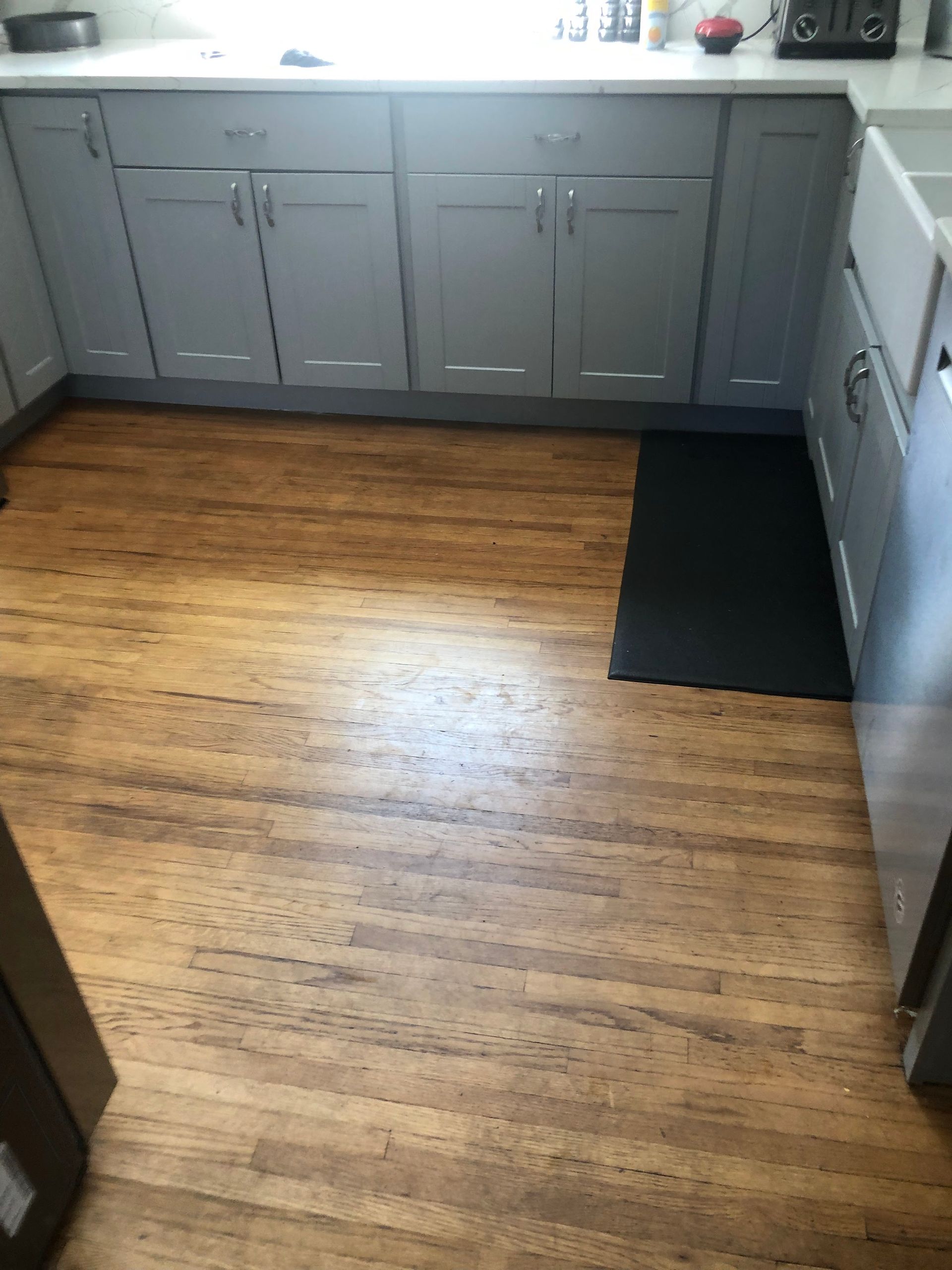 Kitchen with gray cabinets, wood floor, and a black mat by the sink.