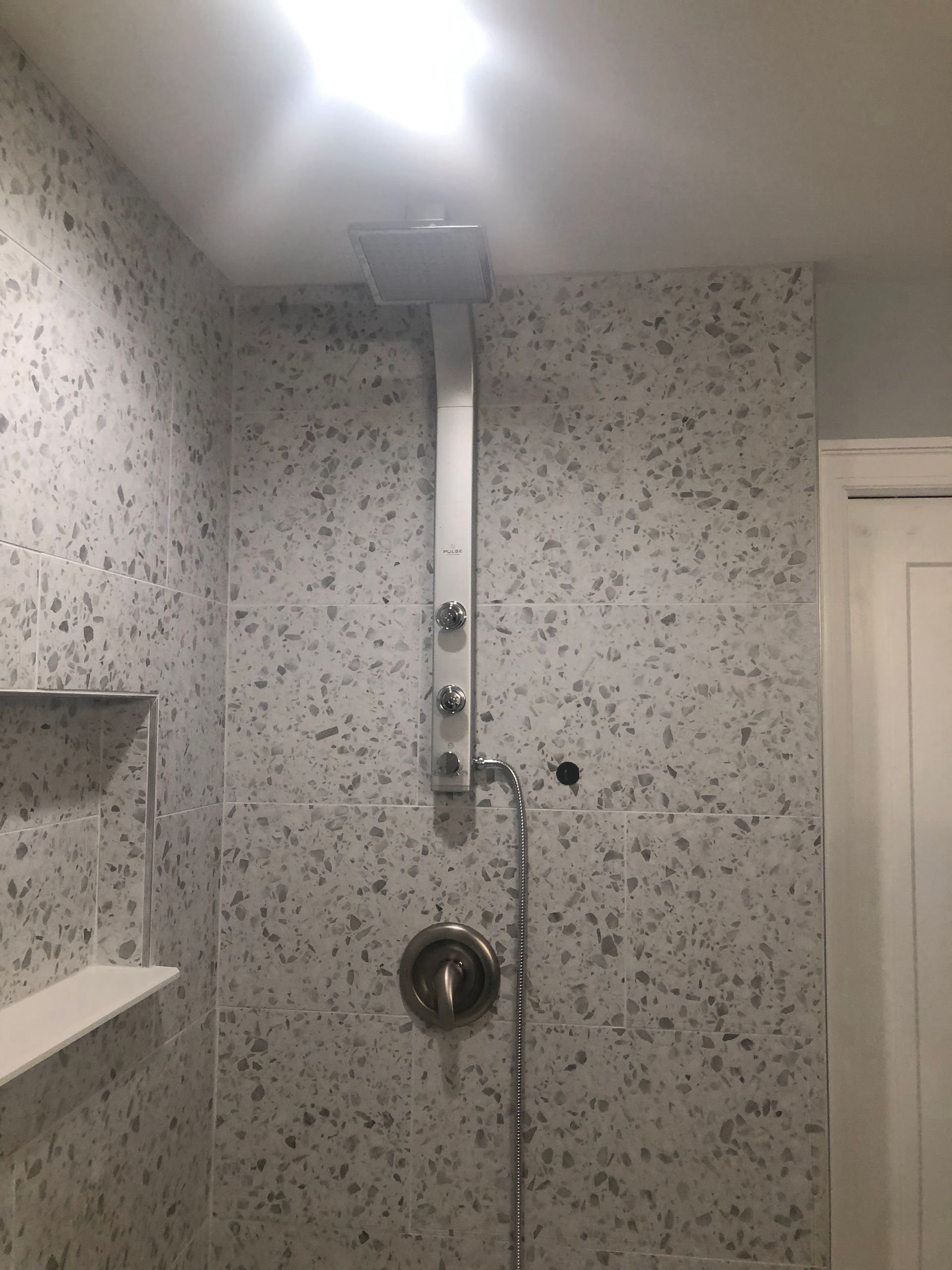 Bathroom shower with gray speckled tile, handheld showerhead, and overhead rain shower.