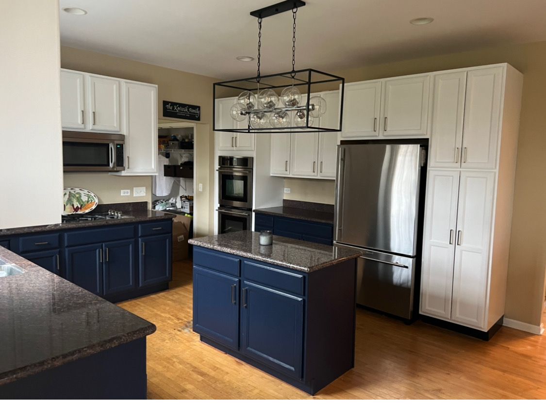 Modern kitchen with white cabinets, blue island, stainless steel appliances, and hanging light fixture