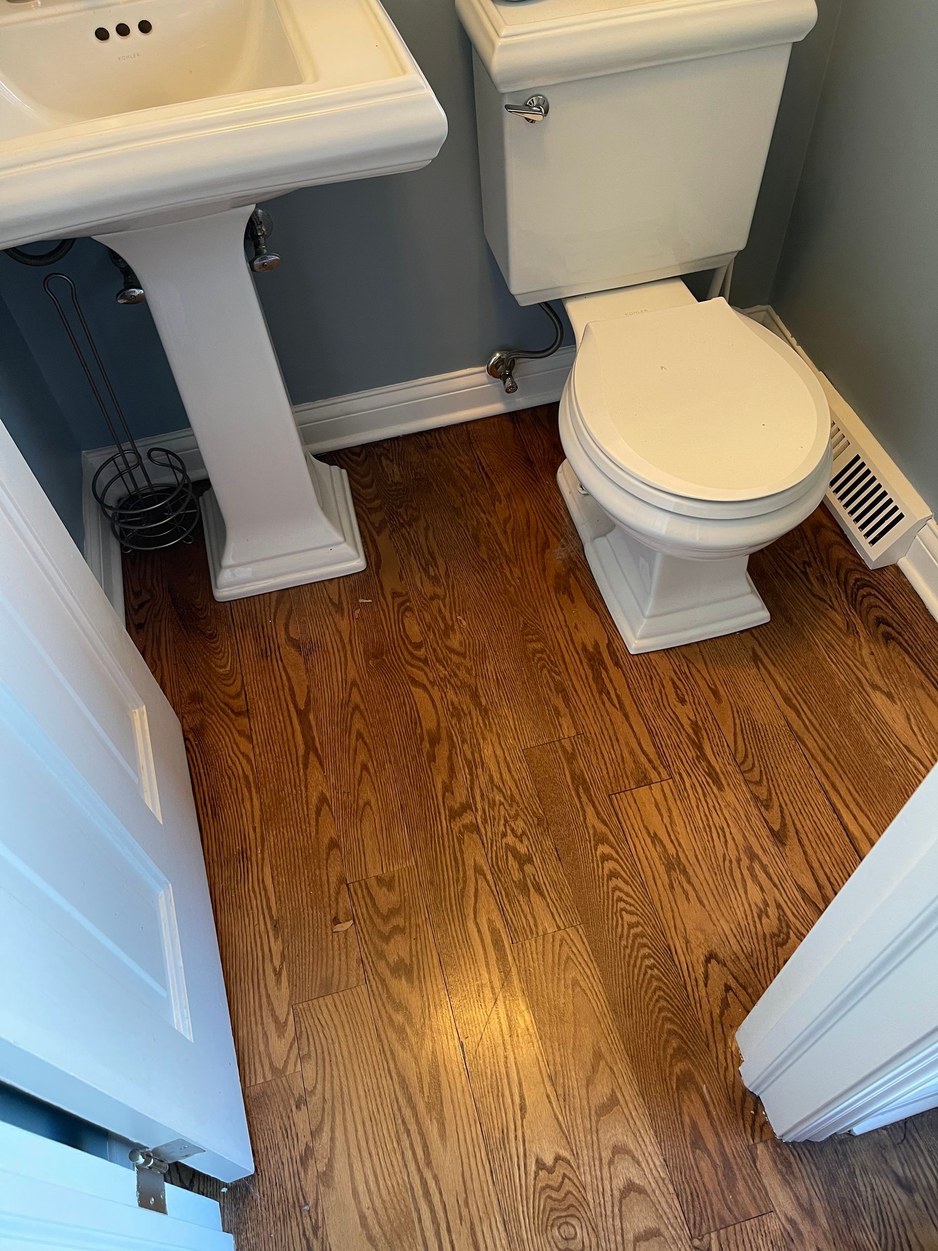 Small bathroom with a toilet, pedestal sink, white trim, and wood-look floor.