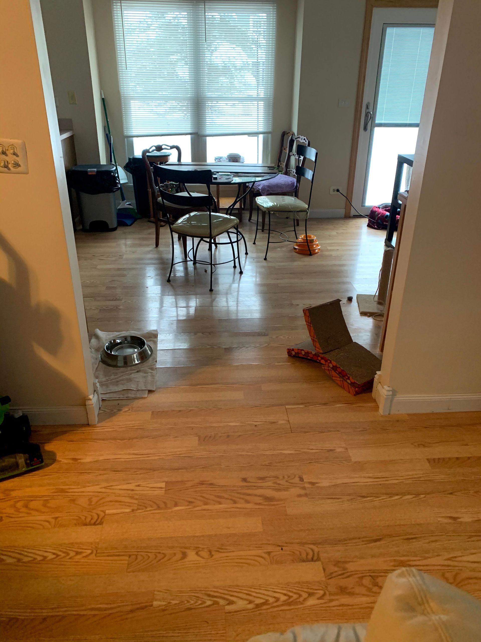 Messy dining room with scattered toys, a table and chairs by bright windows, and hardwood floors