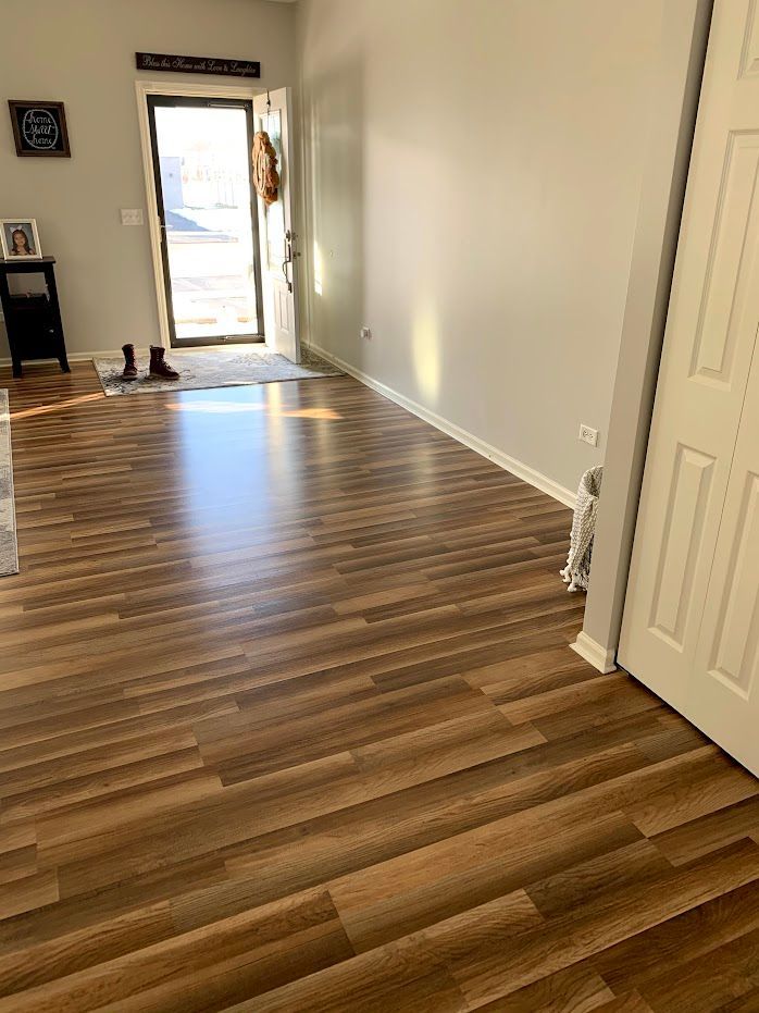 Empty room with wood-look flooring, white walls, and open front door with daylight streaming in