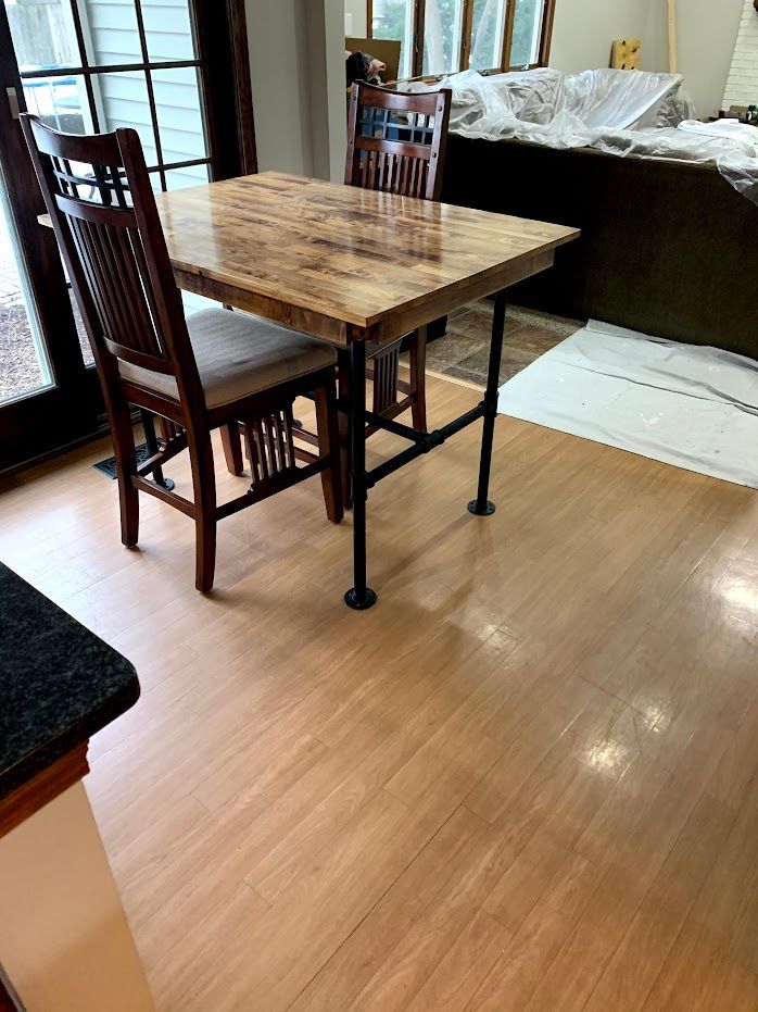 Wooden dining table with two chairs in a bright room beside a bed and open doorway.