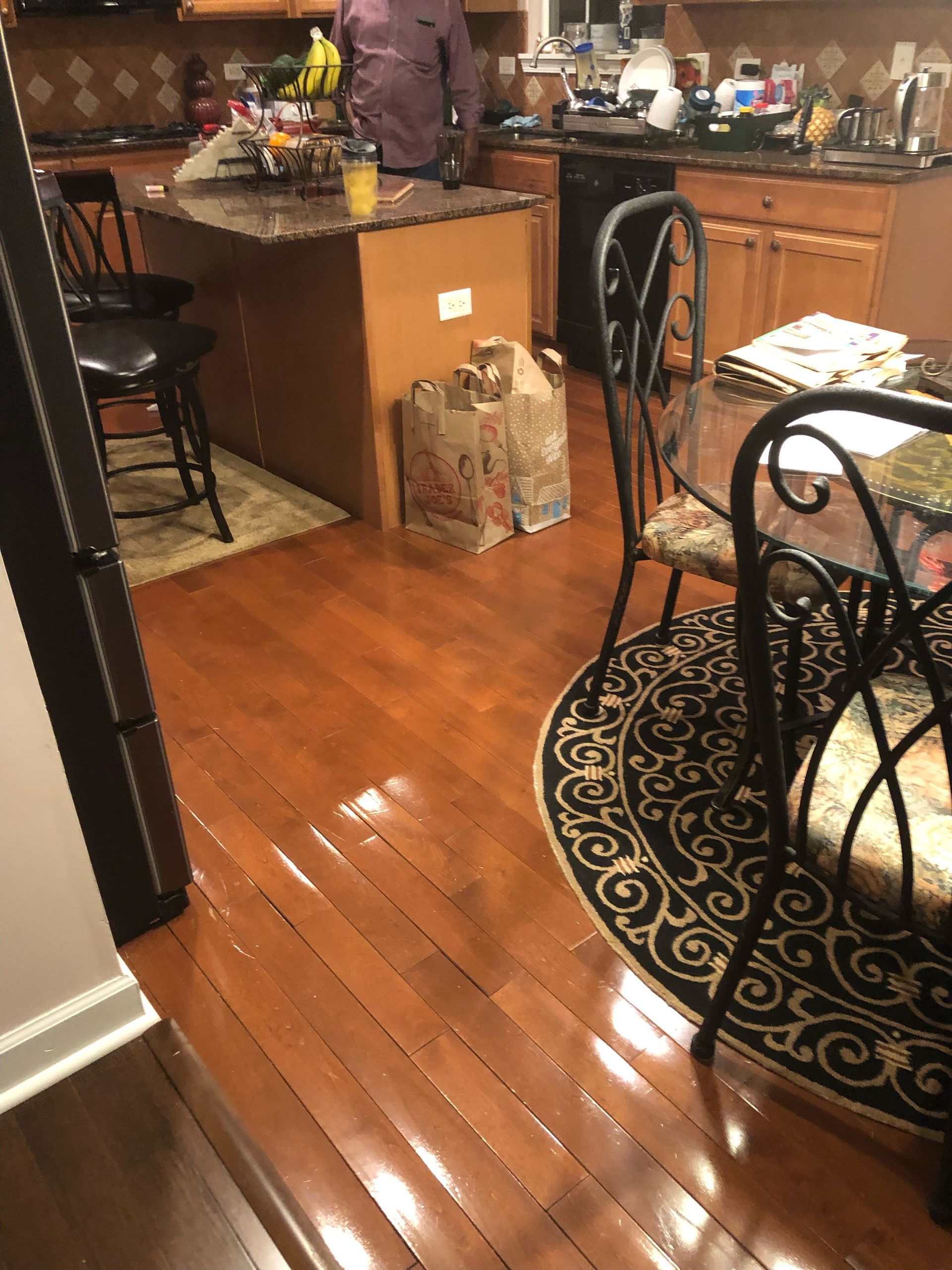 Kitchen with hardwood floor, island, chairs, and a person standing near the counter