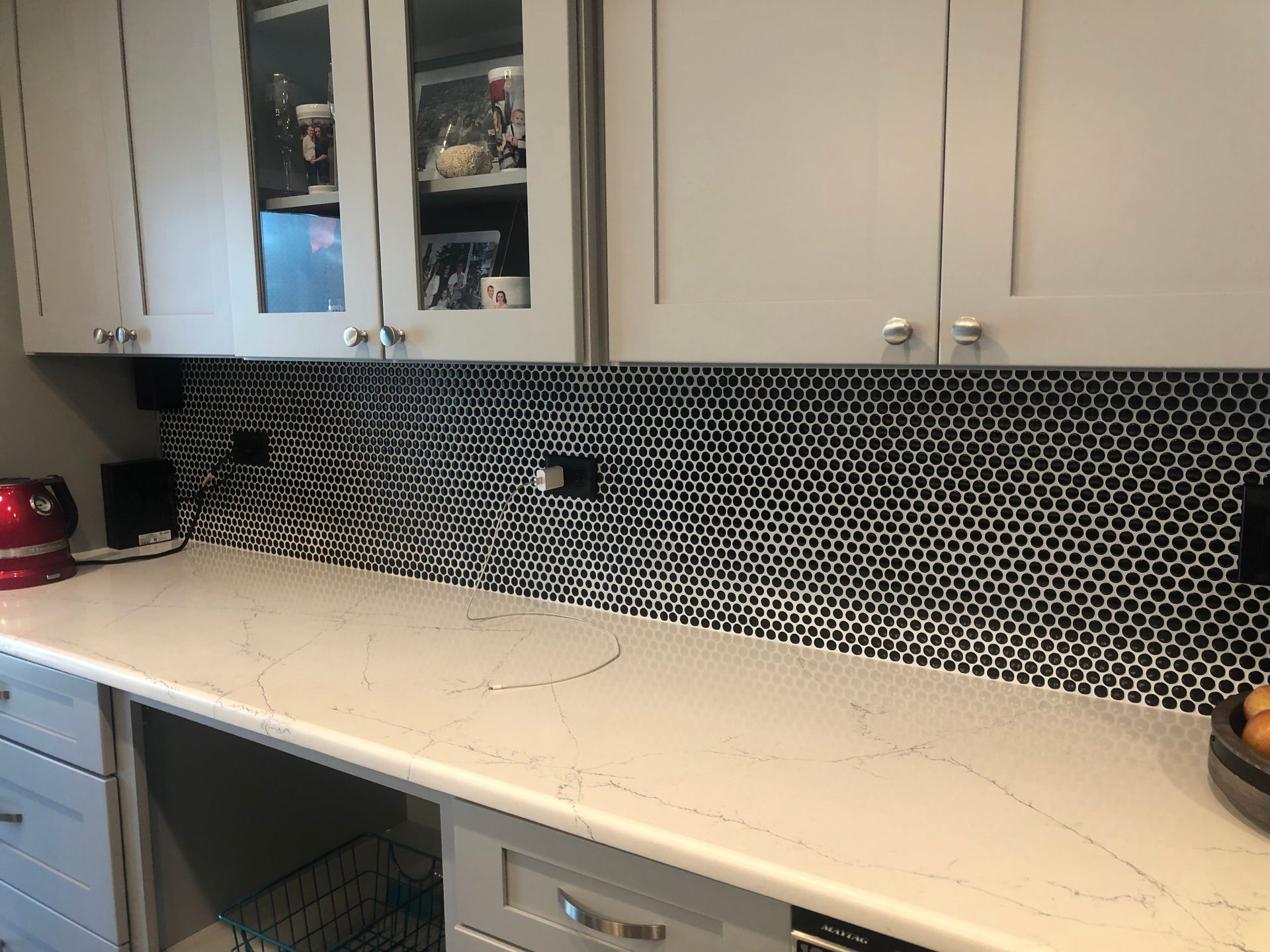 White kitchen countertop with black mosaic backsplash and light cabinets, including a red kettle and some decor