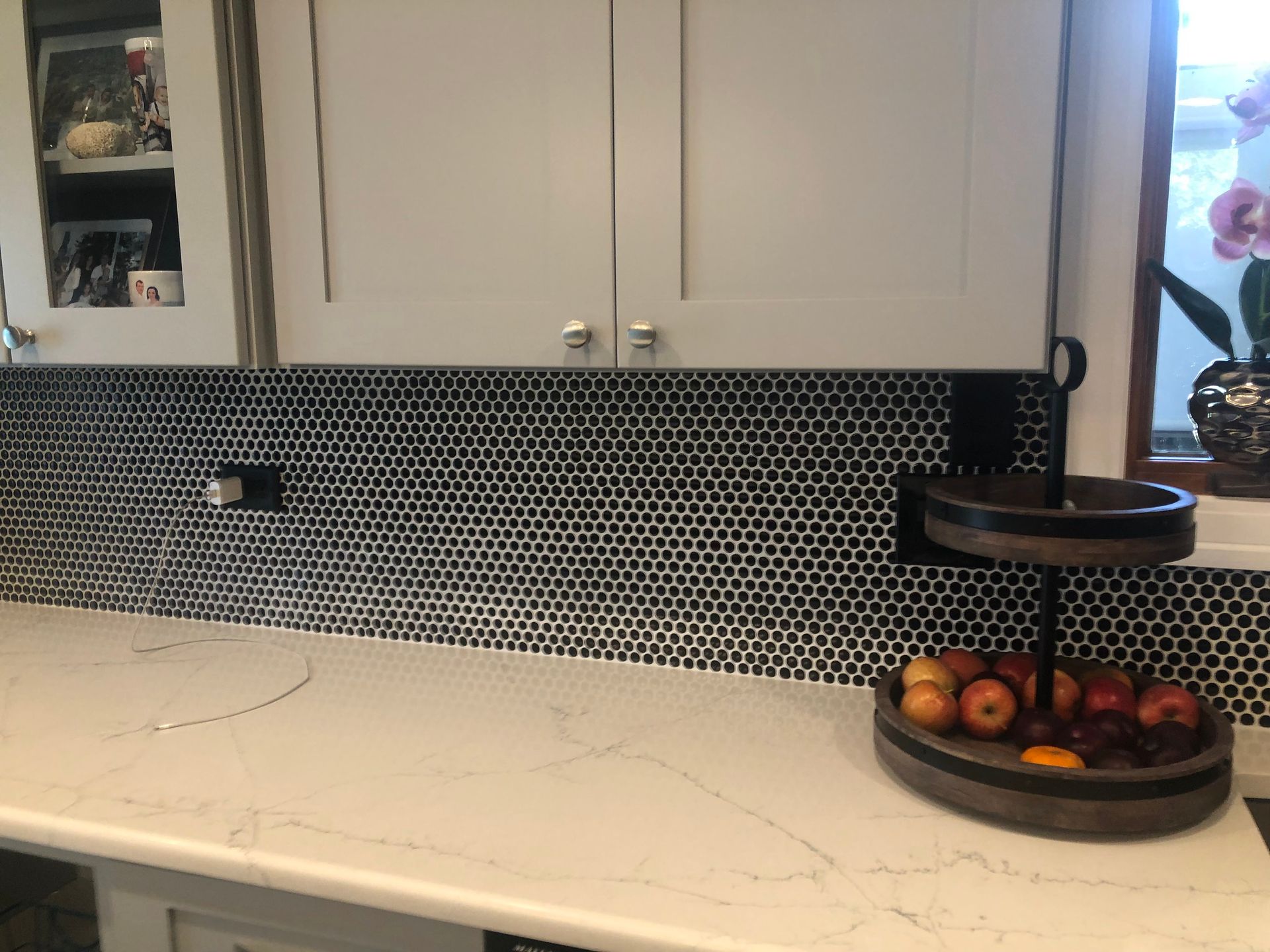 Kitchen countertop with black-and-white mosaic backsplash, white cabinets, and a fruit bowl on the right.