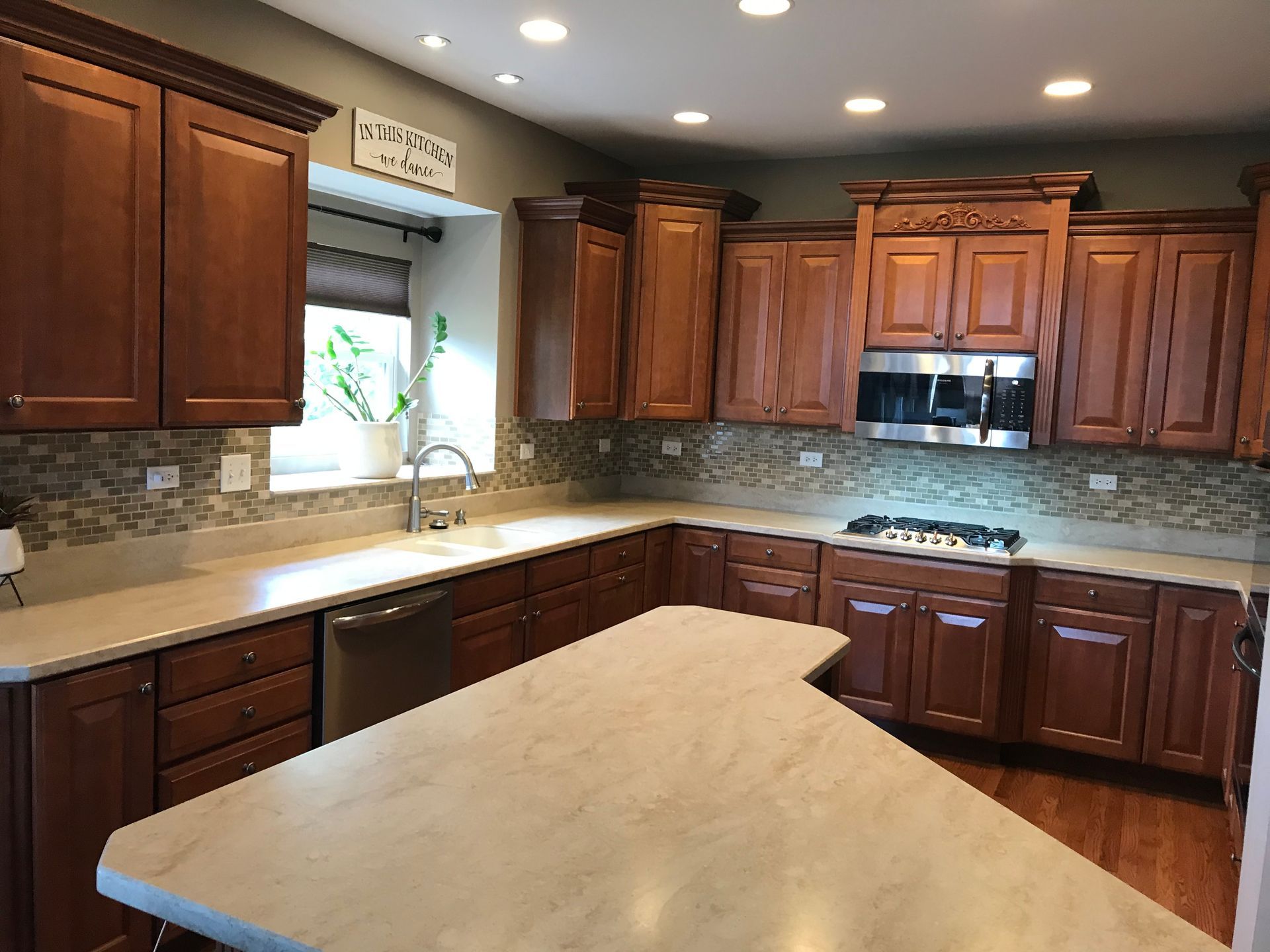 Modern kitchen with wooden cabinets, beige countertops, island, and stainless-steel appliances