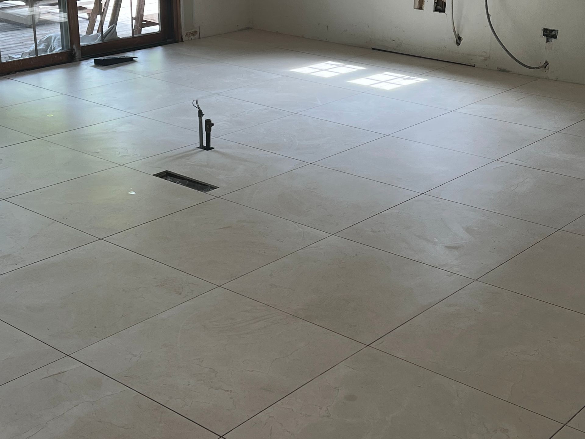 Empty tiled room with unfinished floor tiles, a floor pipe, and sunlight near windows