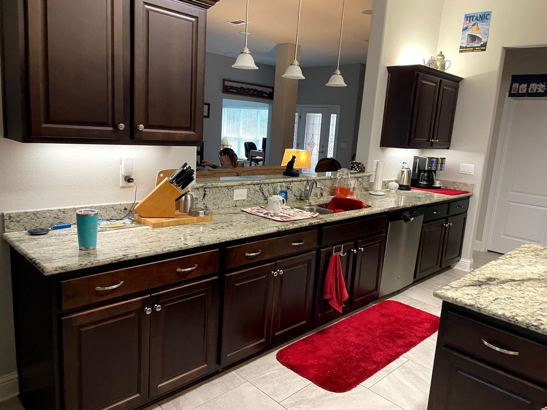 Kitchen with dark wood cabinets, granite counters, red rug, and pendant lights over the island.