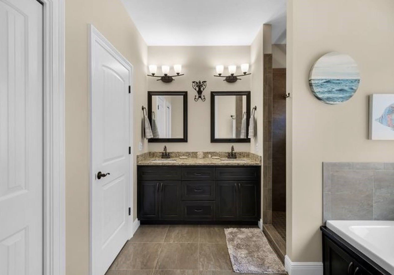 Bathroom vanity with double sinks, black cabinets, mirrors, and wall sconces in a bright hallway.