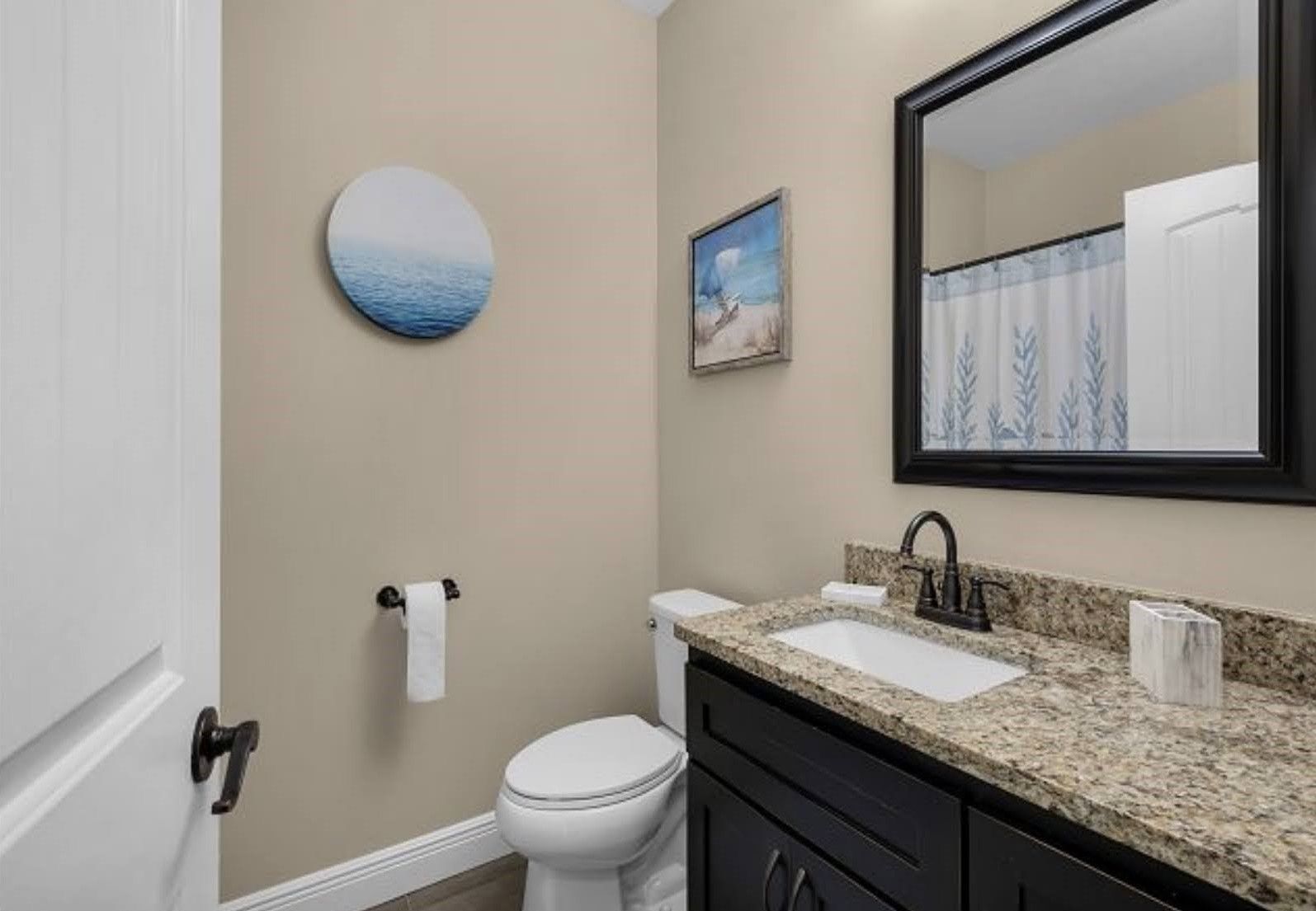 Small bathroom with toilet, granite vanity, sink, mirror, and shower curtain.