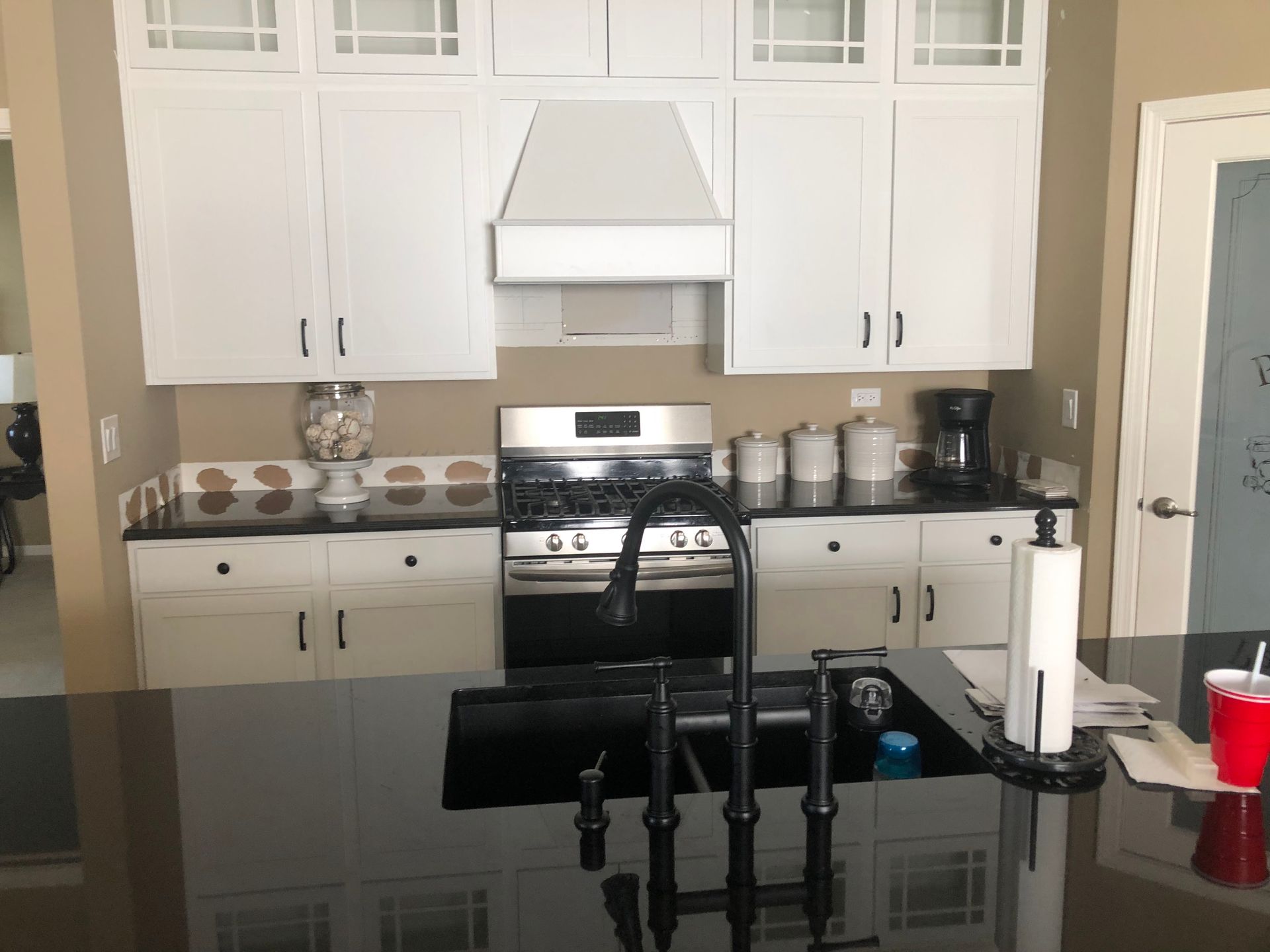 Modern kitchen with white cabinets, stainless stove, black island countertop, and sink faucet in foreground