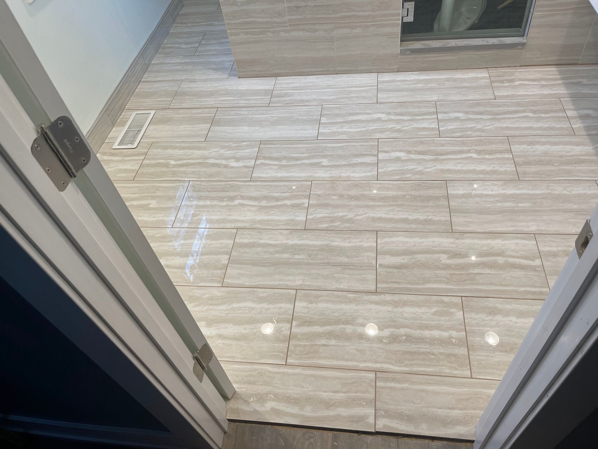 Open doorway to a bathroom with light beige tile flooring and a walk-in shower visible ahead