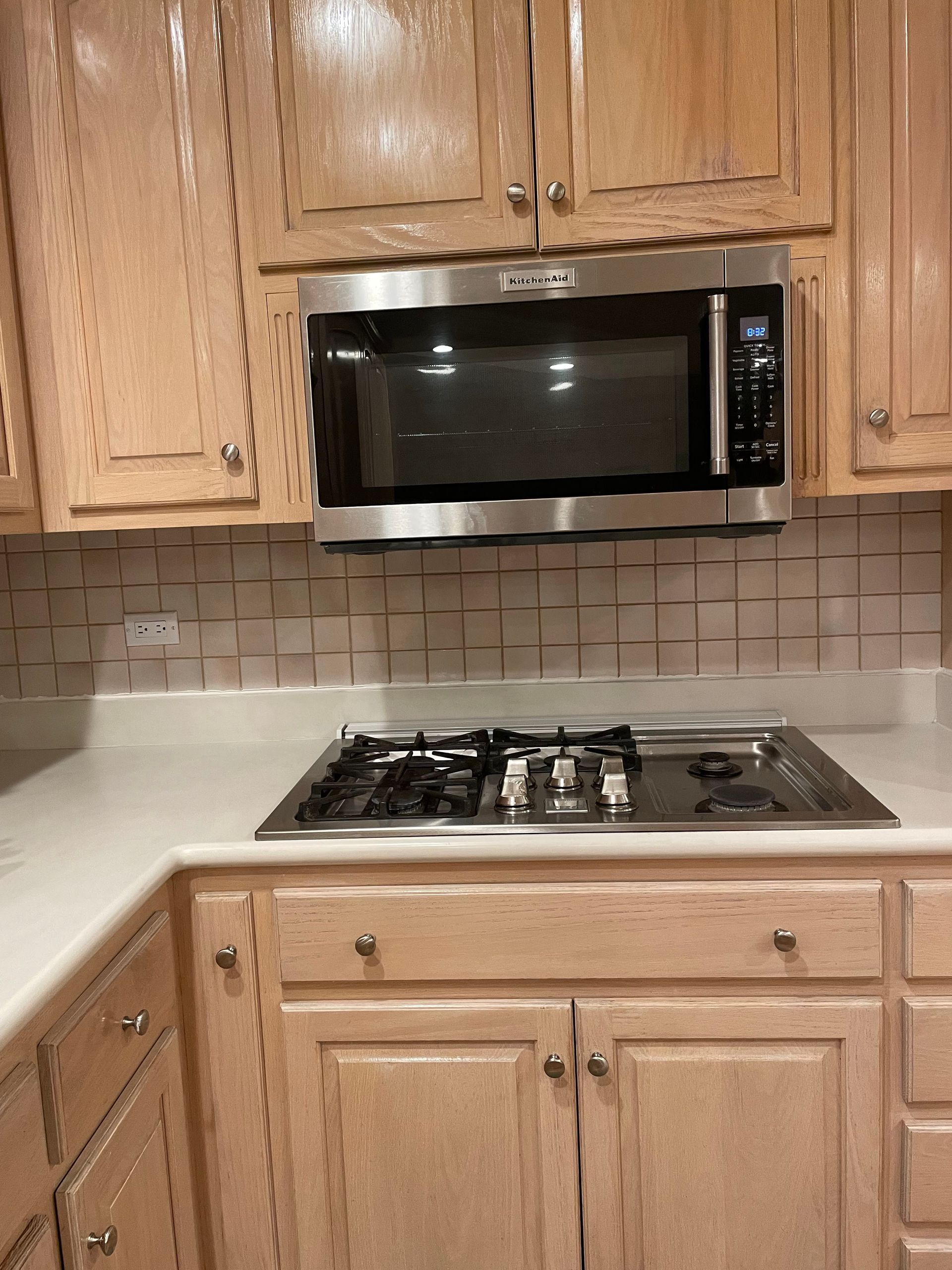 Kitchen with wood cabinets, a black microwave, and a gas cooktop on a light countertop.