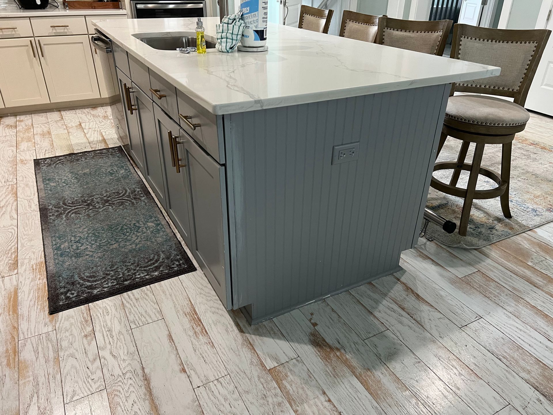 Kitchen island with white countertop, gray paneled sides, and stools on a light wood floor
