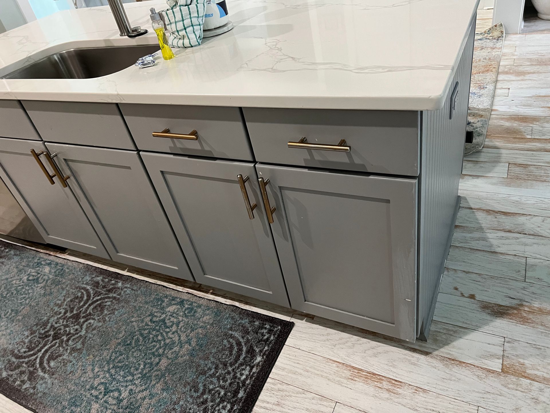 Gray kitchen island with white countertop, sink, and brass handles beside a patterned rug