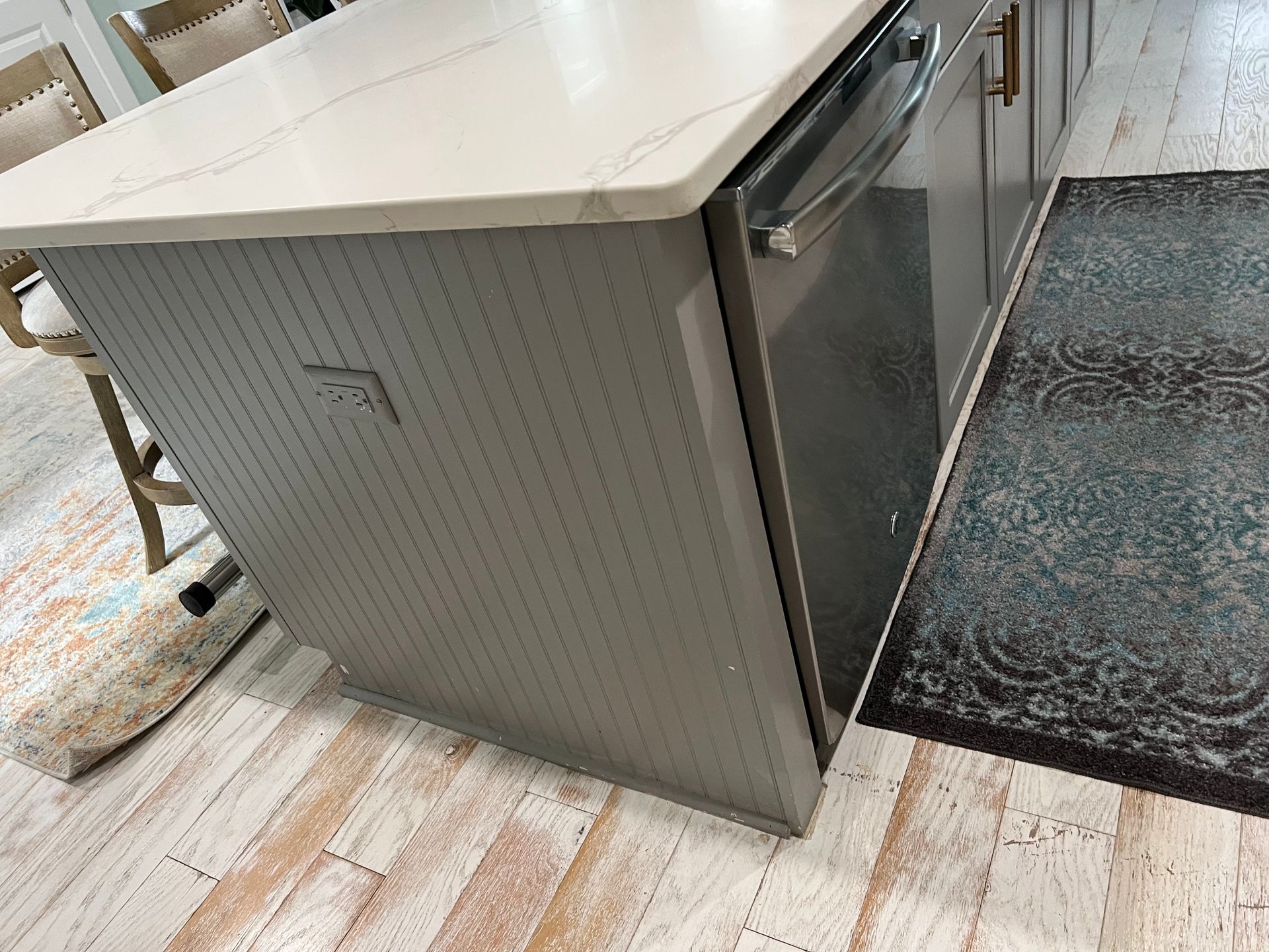 Stainless steel kitchen island on a light wood floor beside a dark rug, viewed at an angle