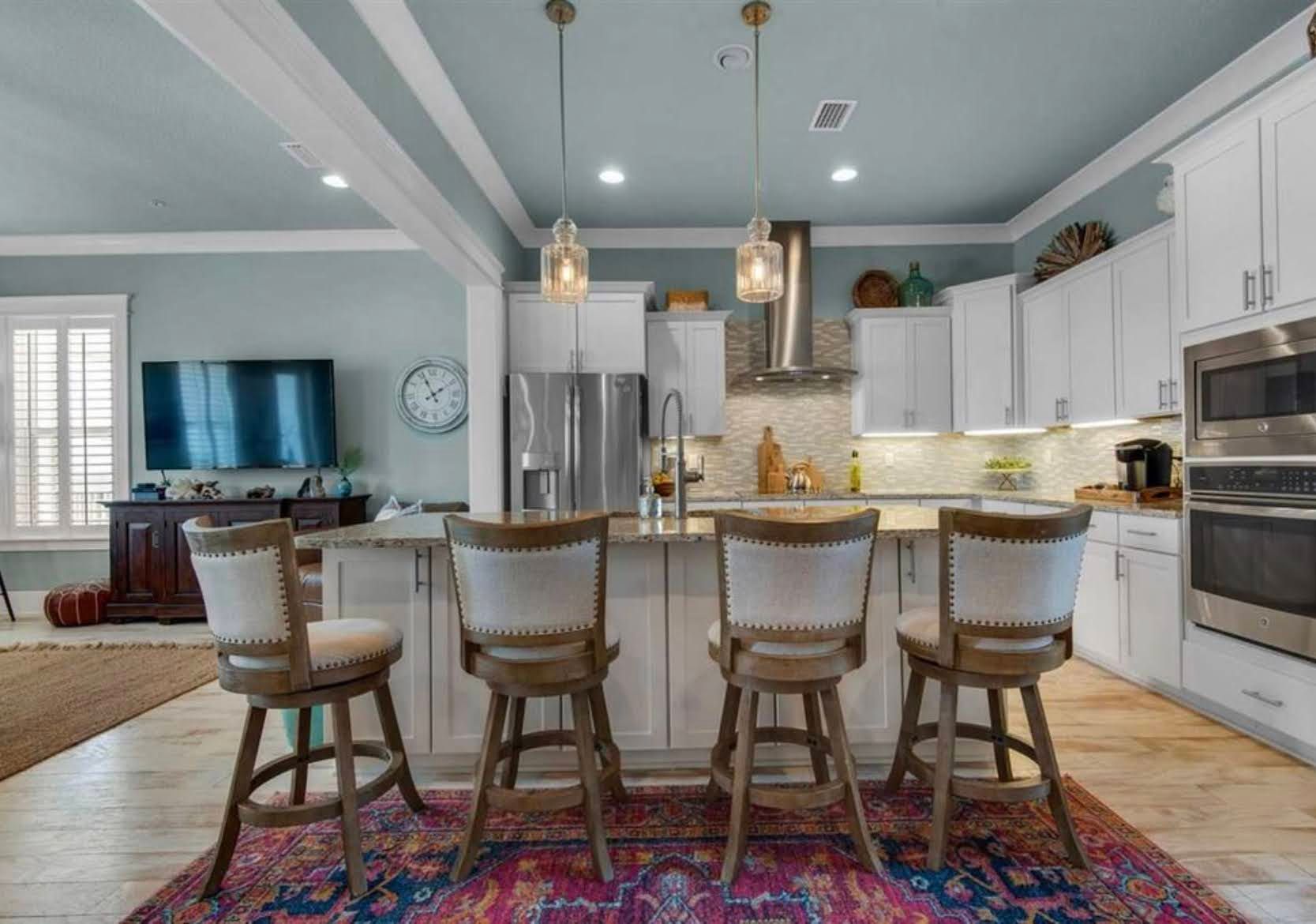 Bright modern kitchen with white cabinets, large island, four stools, and colorful rug.