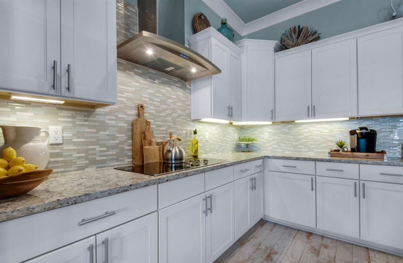 Modern white kitchen with gray countertops, stainless hood, tile backsplash, and wood flooring
