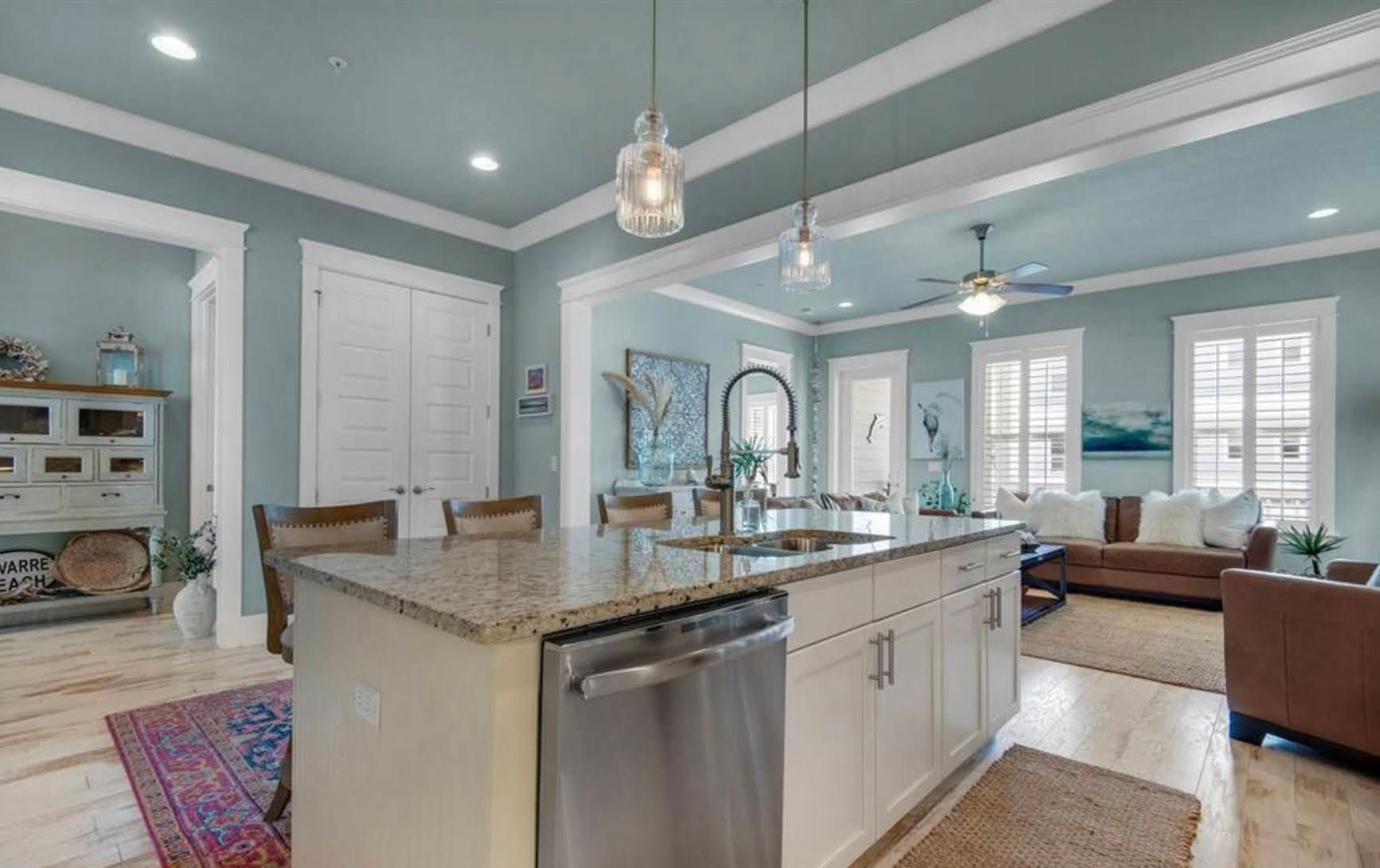 Bright open kitchen and living area with teal walls, white cabinets, granite island, and wood furniture