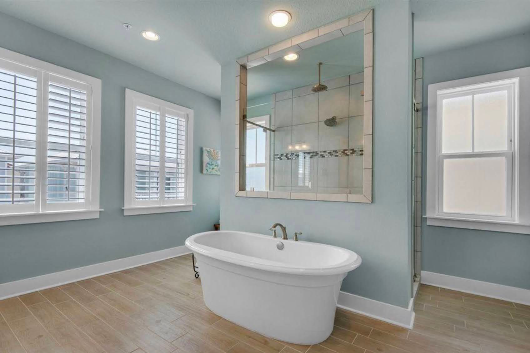 Bright modern bathroom with a freestanding tub, large mirror, and light blue walls