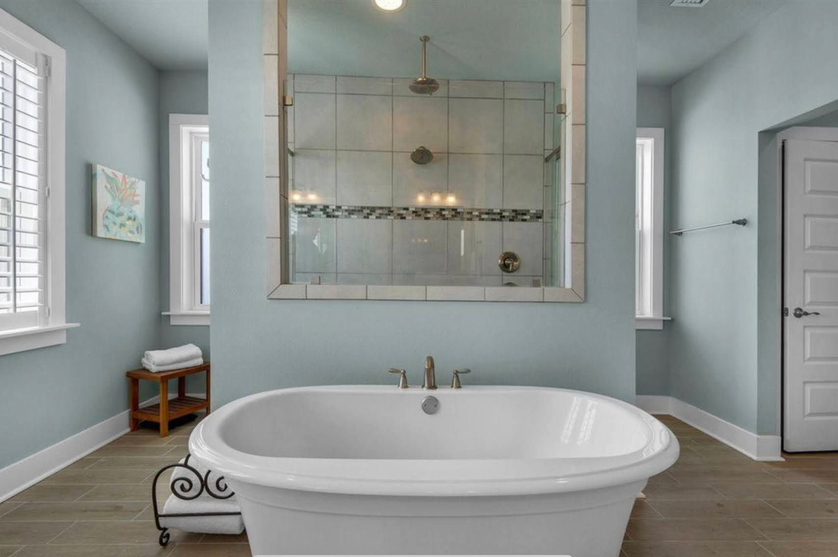 Bright modern bathroom with a freestanding tub, glass shower, light blue walls, and wood floor