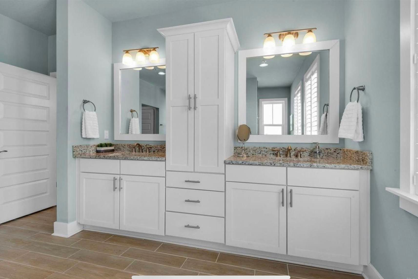 Bathroom vanity with double sinks, mirrors, and white cabinets in a light gray room