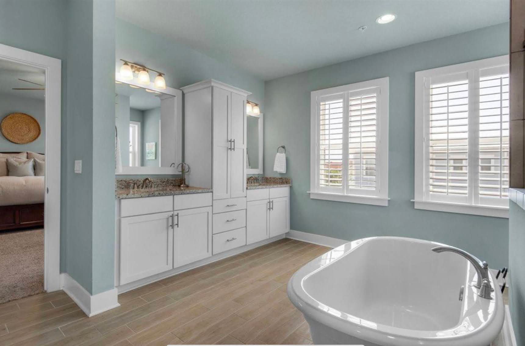 Bright bathroom with white vanity, tiled floor, large windows, and a freestanding tub