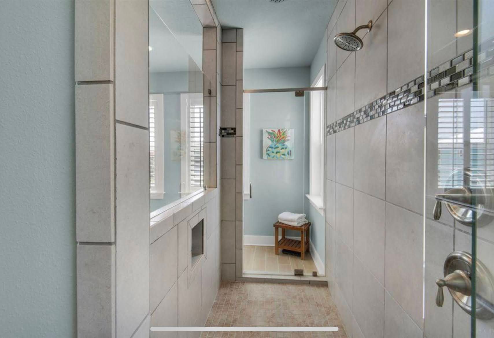 Bright tiled bathroom with glass shower, sink, and toilet in a narrow, modern layout