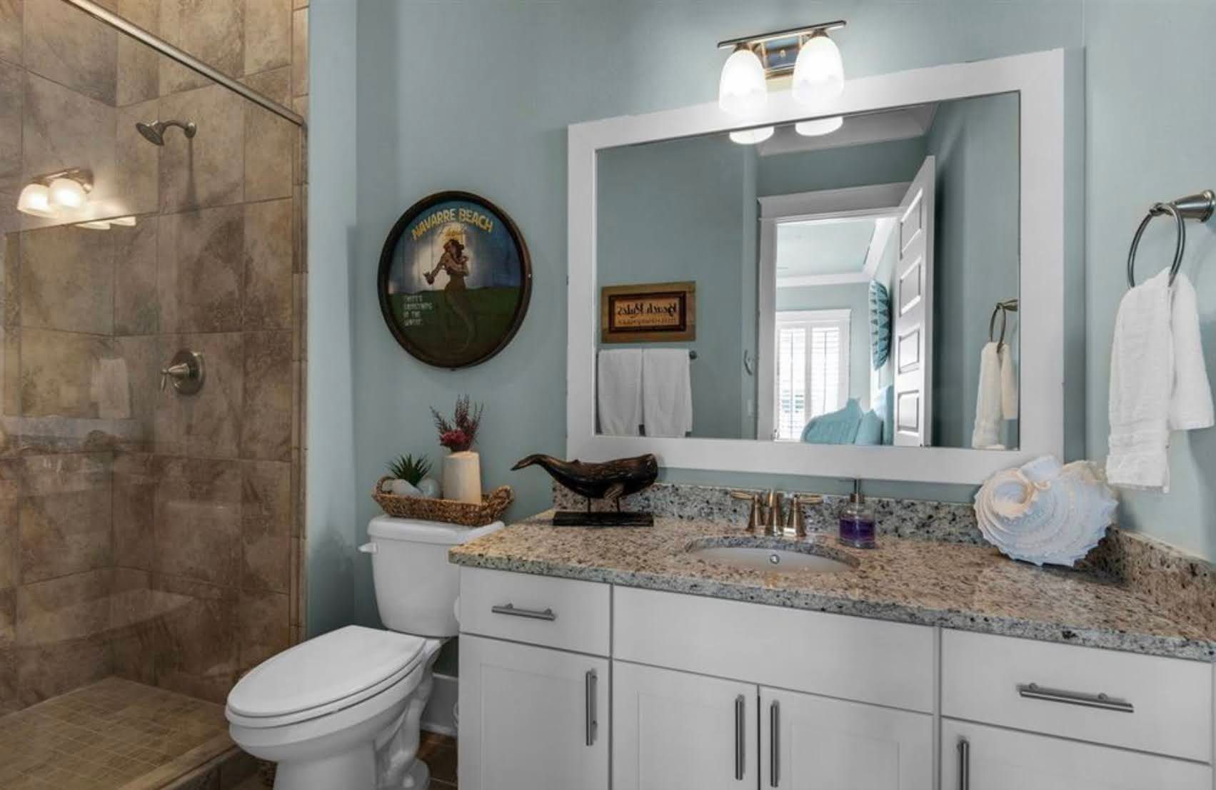 Modern bathroom with white vanity, granite countertop, mirror, and glass shower stall