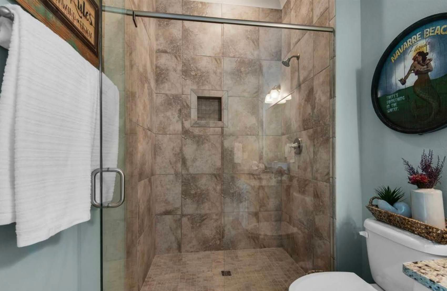 Small bathroom shower with beige tile walls, glass door, towel, and shelf decor