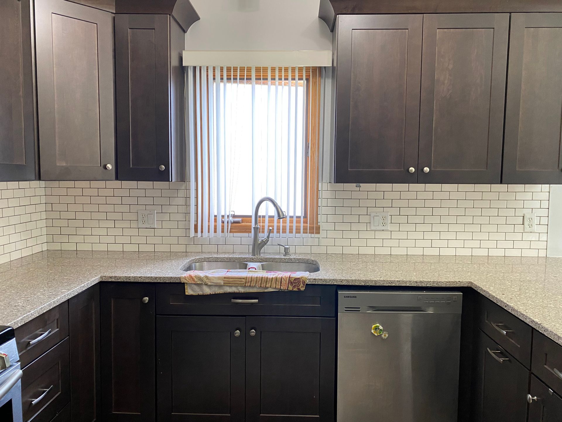 Modern kitchen with dark cabinets, white countertops, subway tile backsplash, and a window over the sink