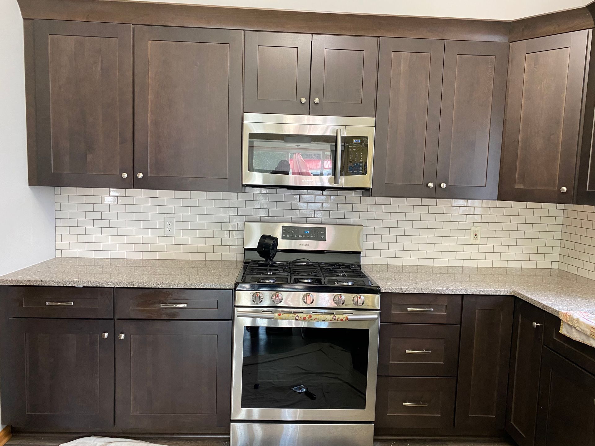 Modern kitchen with dark wood cabinets, stainless steel stove and microwave, and light tile backsplash