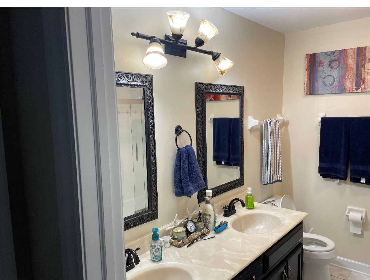 Bathroom vanity with two mirrors, lights, sink, towels, and a toilet in the background