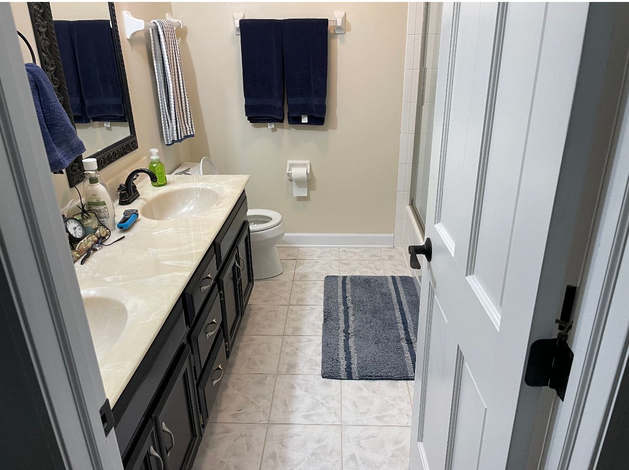 Small bathroom with a white sink, gray vanity, dark towels, and a striped rug on tile floor.